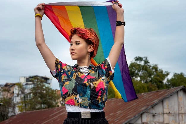 Vista frontal pelirroja persona no binaria sosteniendo una bandera lgbt