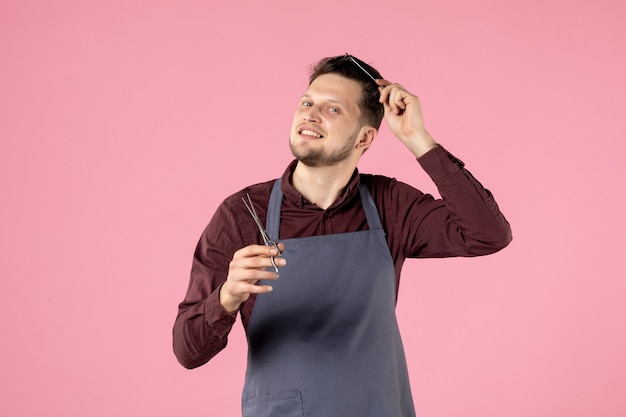 Vista frontal de la peluquería masculina con cepillo y tijeras cuidando su cabello sobre fondo de color rosa