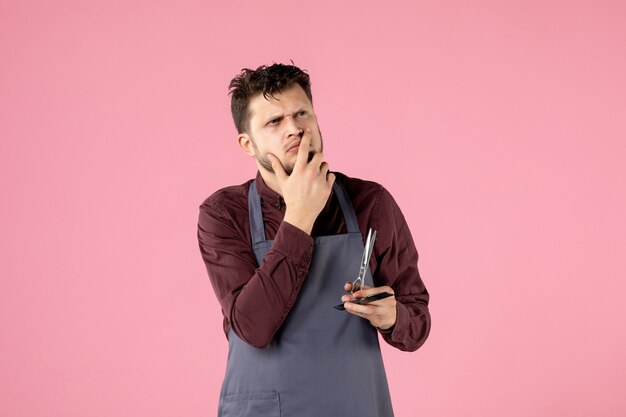 Vista frontal de la peluquería masculina con cepillo y tijeras pensando en fondo de color rosa