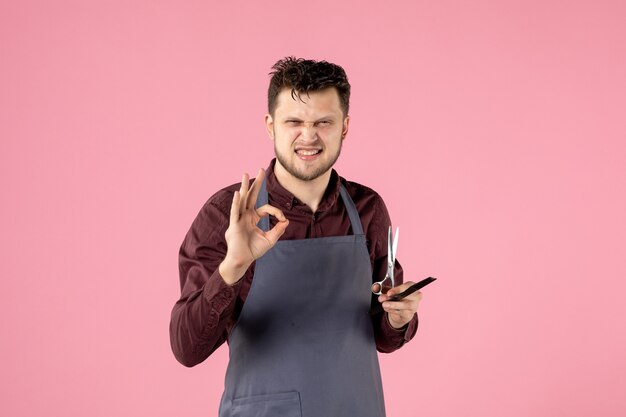 Vista frontal de la peluquería masculina con cepillo y tijeras sobre fondo de color rosa