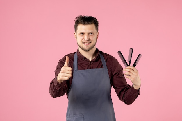 Foto gratuita vista frontal del peluquero masculino con cepillos para el cabello sobre fondo de color rosa