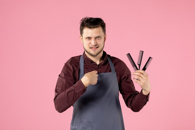 Vista frontal del peluquero masculino sosteniendo cepillos para el cabello sobre fondo de color rosa