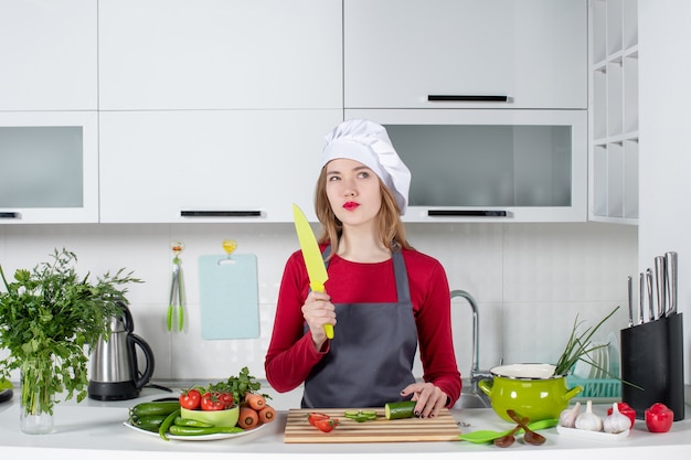 Vista frontal pensativa cocinera en delantal con cuchillo