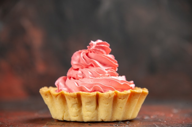 Vista frontal pequeña tarta con crema pastelera rosa sobre mesa rojo oscuro