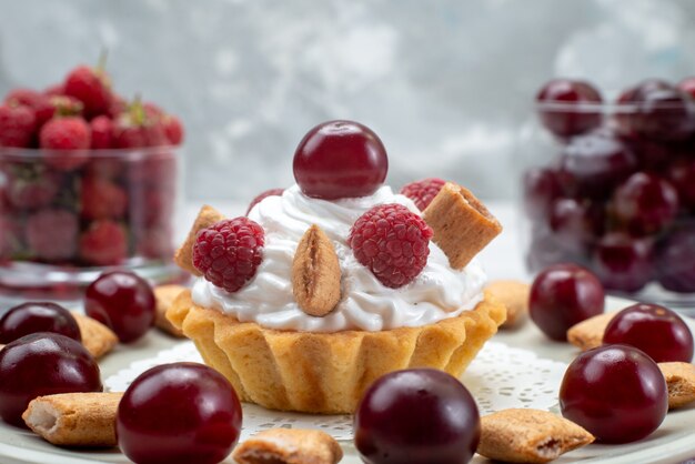 Vista frontal pequeña tarta cremosa con frambuesas y galletas pequeñas en el escritorio de luz blanca, tarta de frutas crema de bayas dulces