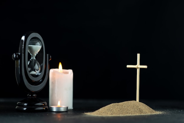 Vista frontal de la pequeña tumba con reloj de arena y velas en la oscuridad