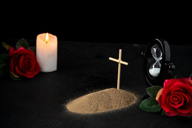 Vista frontal de la pequeña tumba con velas y rosas rojas sobre negro