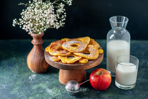 Vista frontal pequeñas y deliciosas tartas en forma de anillo de piña con leche en una tarta de frutas oscuras pastel de pastelería hotcake color hornear