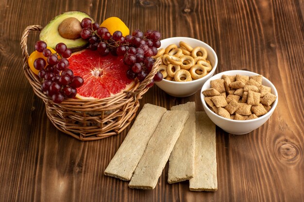 Vista frontal pequeñas galletas dulces con diferentes frutas en el escritorio marrón