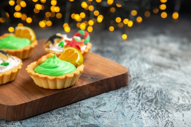 Vista frontal pequeñas tartas en adornos de Navidad de tabla de cortar en luces de Navidad de superficie oscura