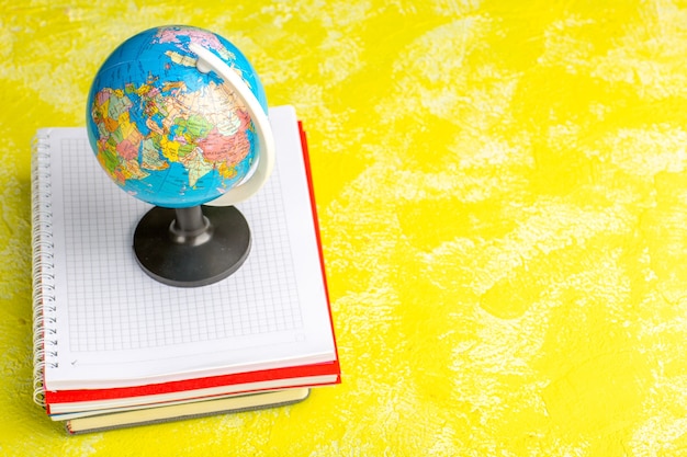 Foto gratuita vista frontal del pequeño globo con cuadernos sobre superficie amarilla