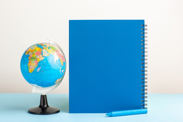 Vista frontal pequeño globo terráqueo con cuaderno azul sobre escritorio azul