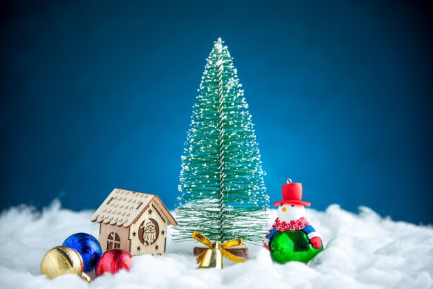 Vista frontal pequeño muñeco de nieve árbol de Navidad casa de madera juguetes de bolas en superficie aislada azul