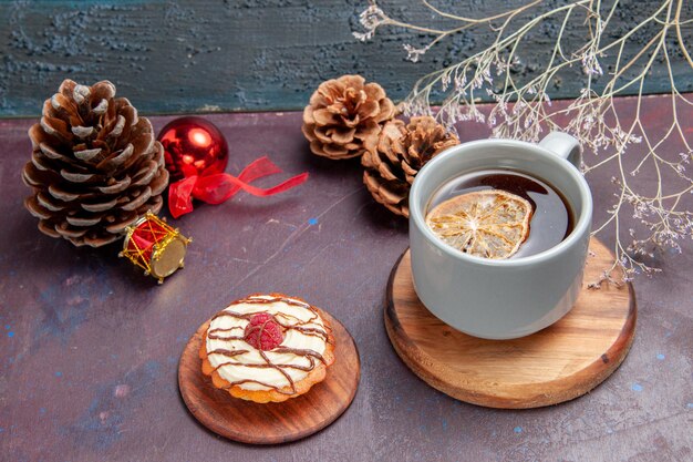 Vista frontal pequeño pastel cremoso con taza de té sobre fondo oscuro pastel de galleta pastel de galleta de azúcar dulce