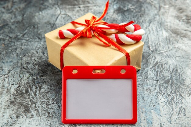 Vista frontal pequeño regalo atado con cinta roja tarjetero de dulces navideños en gris