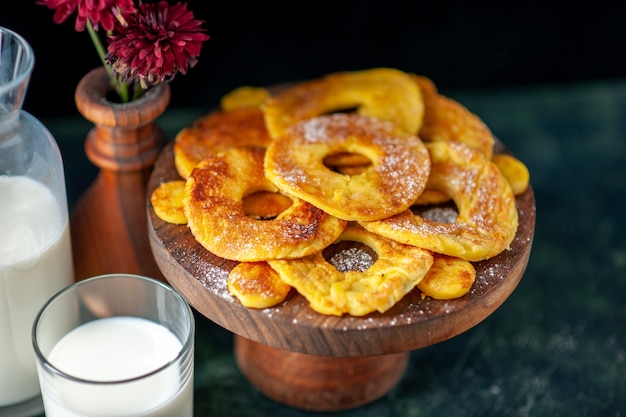 Vista frontal pequeños deliciosos pasteles en forma de anillo de piña con leche en la superficie oscura