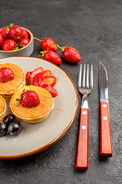 Vista frontal pequeños panqueques deliciosos con frutas en la superficie oscura pastel pastel de frutas