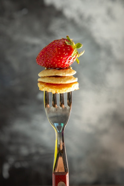 Vista frontal pequeños panqueques con fresa en tenedor y pastel de escritorio gris comida de frutas