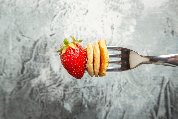 Vista frontal de pequeños panqueques con fresa en un tenedor y postre de fruta de pastel de superficie ligera