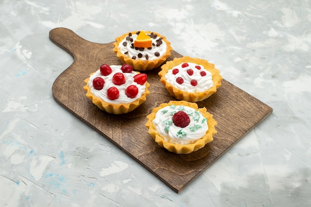 Vista frontal de pequeños pasteles de crema con frutas en el dulce de azúcar de escritorio gris claro