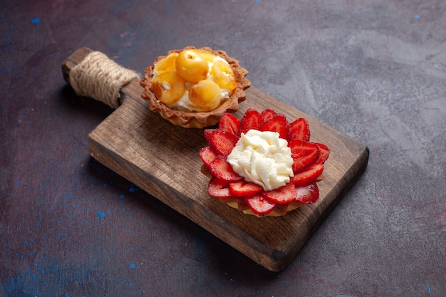 Vista frontal de pequeños pasteles cremosos con frutas en rodajas sobre una superficie oscura