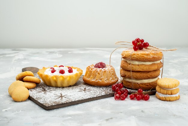 Vista frontal de pequeños pasteles d con crema y galletas de sándwich en la superficie ligera dulce de azúcar