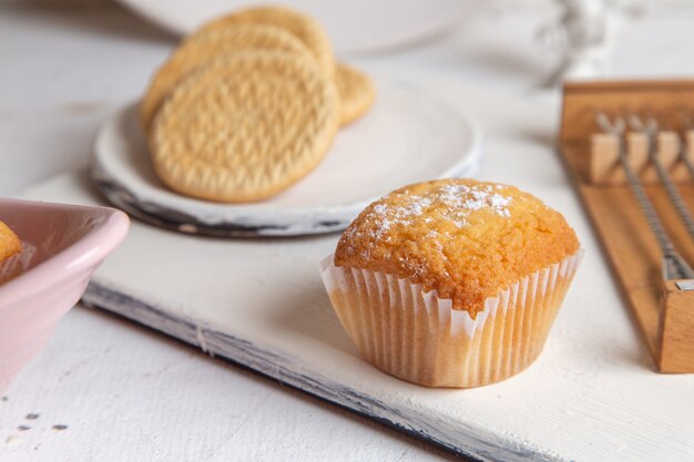 Vista frontal de pequeños pasteles deliciosos con azúcar en polvo y galletas en el escritorio blanco