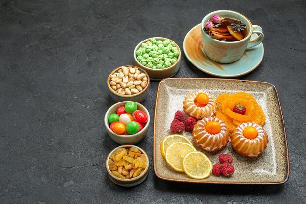 Vista frontal pequeños pasteles deliciosos con dulces frutas y nueces en el espacio gris