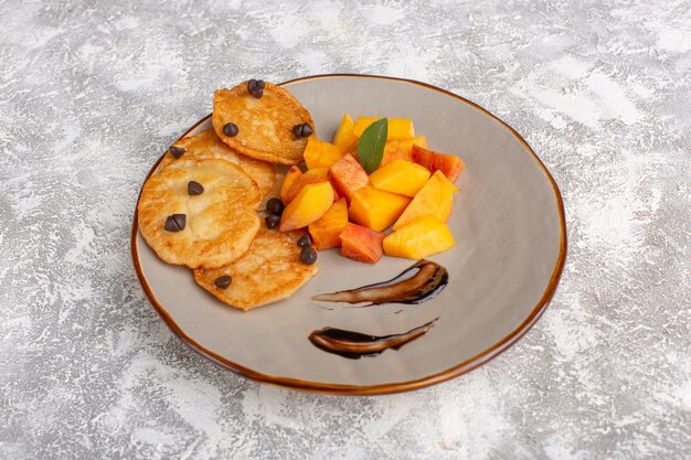 Vista frontal de pequeños pasteles de galleta dentro de la placa con melocotones frescos en rodajas en la mesa de luz, pastel de galleta pastelería dulce hornear