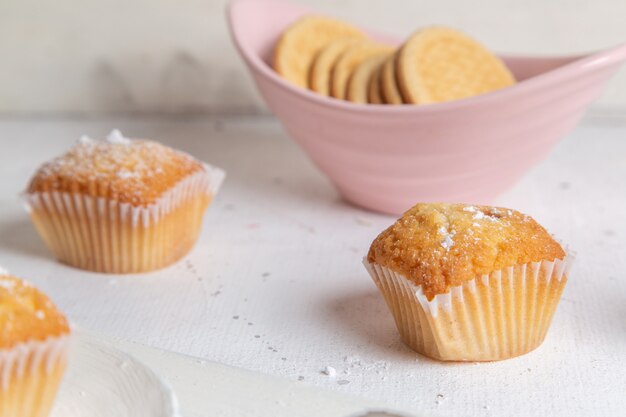 Vista frontal de pequeños pasteles horneados y deliciosos con galletas en la superficie blanca