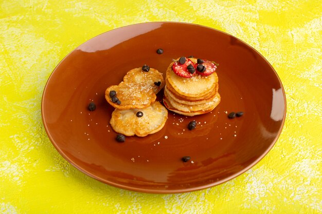 Vista frontal de pequeños pasteles horneados con frutos secos en la mesa amarilla, pasteles de azúcar dulce de bayas de frutas