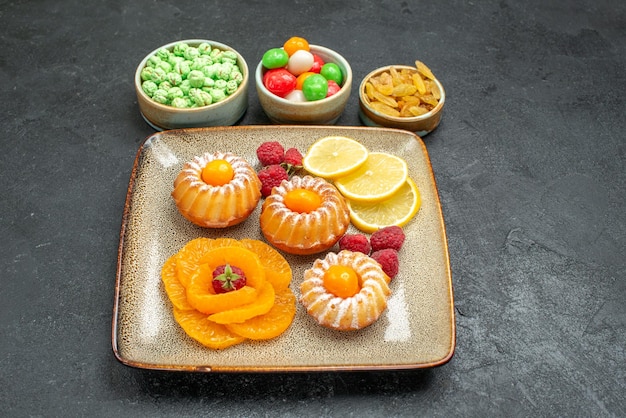 Vista frontal de pequeños pasteles con rodajas de limón, mandarinas y dulces en el espacio oscuro