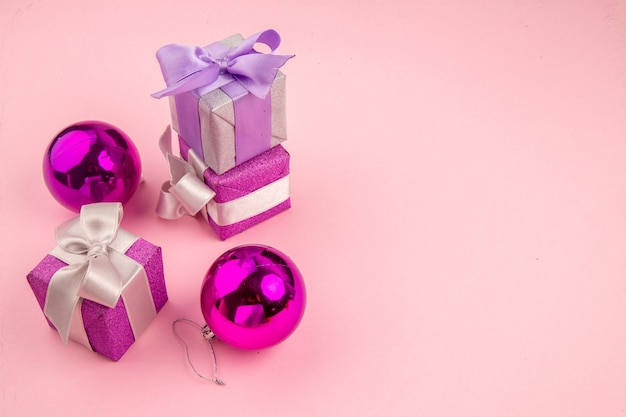 Vista frontal pequeños regalos con juguetes de árbol de Navidad en la mesa rosa