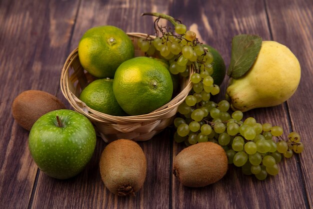 Vista frontal de pera con kiwi mandarinas manzanas y uvas en una canasta sobre una pared de madera