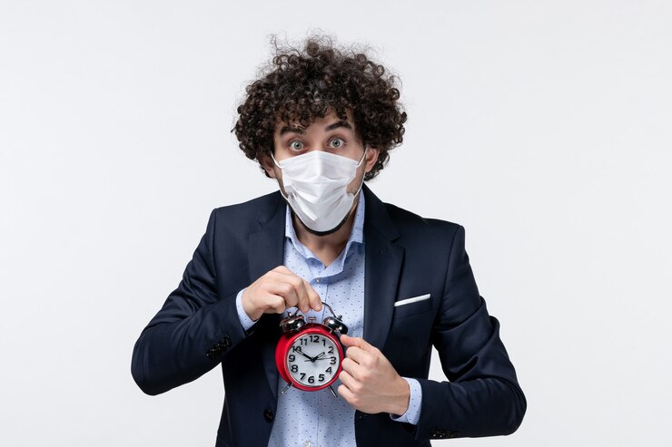 Foto gratuito vista frontal de la persona de negocios sorprendida conmocionada en traje y con su máscara sosteniendo el reloj