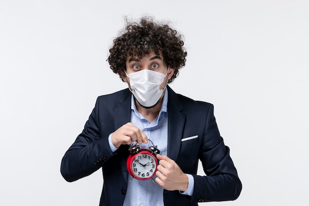 Vista frontal de la persona de negocios sorprendida conmocionada en traje y con su máscara sosteniendo el reloj