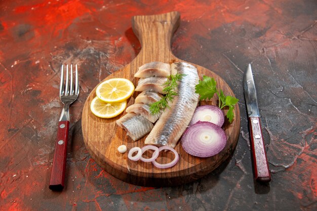 Vista frontal de pescado fresco en rodajas con aros de cebolla y limón en un bocadillo oscuro color carne mariscos