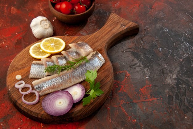 Vista frontal de pescado fresco en rodajas con aros de cebolla y tomates en un bocadillo oscuro color carne mariscos