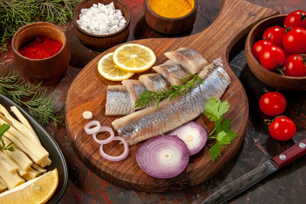 Vista frontal de pescado fresco en rodajas con condimentos y aros de cebolla en mariscos oscuros foto en color snack carne ensalada madura