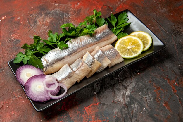 Vista frontal de pescado fresco en rodajas con verduras y cebolla dentro de una sartén negra en un bocadillo oscuro comida de color carne mariscos