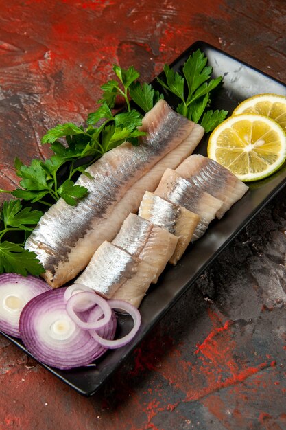 Vista frontal de pescado fresco en rodajas con verduras y cebolla dentro de una sartén negra en un bocadillo oscuro comida de color de carne