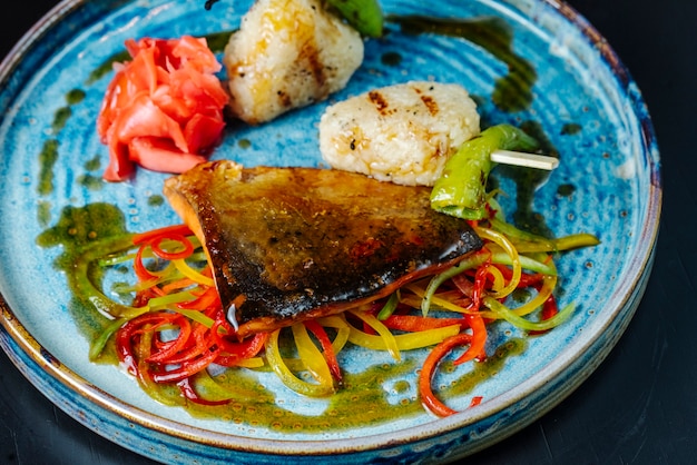 Vista frontal de pescado a la parrilla con salsa y pimiento en un plato