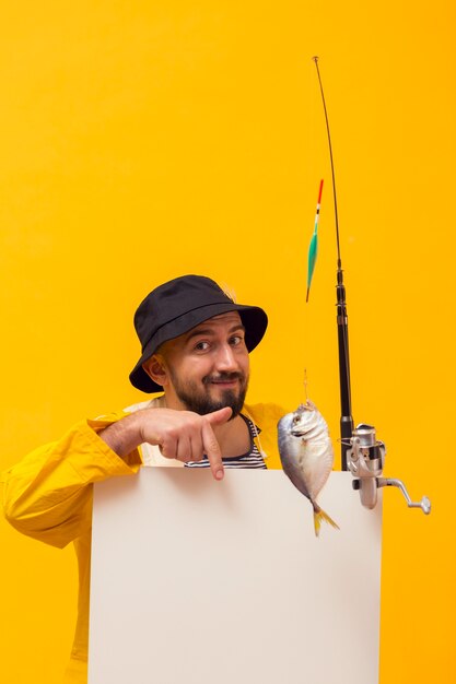 Vista frontal del pescador sosteniendo la caña de pescar y apuntando al cartel en blanco