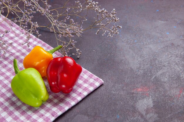 Vista frontal de pimientos frescos de colores sobre la superficie gris pimiento vegetal picante comida caliente