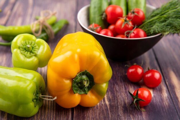 Vista frontal de pimientos con tazón de tomate pepino y eneldo sobre superficie de madera