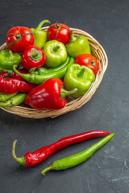 Vista frontal de pimientos y tomates en canasta de mimbre, pimientos picantes sobre fondo oscuro