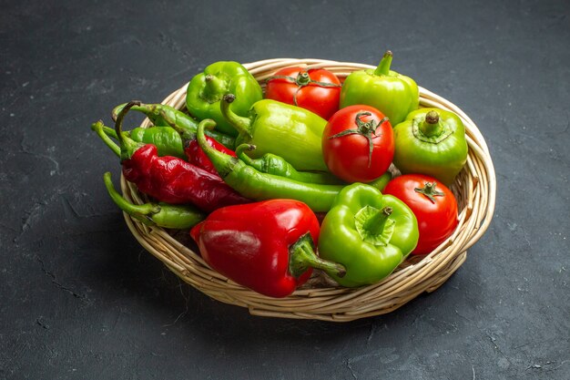 Vista frontal de pimientos y tomates en un tazón de canasta de mimbre sobre fondo oscuro