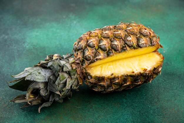 Vista frontal de piña con una pieza cortada de fruta entera en superficie verde