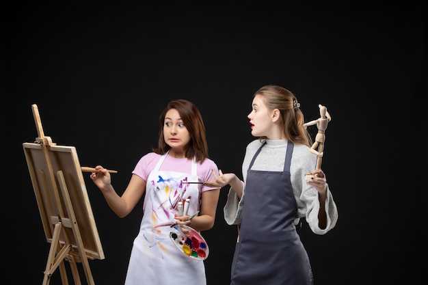 Vista frontal pintores femeninas dibujo figura humana en caballete en pared negra foto color dibujar pinturas trabajo arte artista imagen