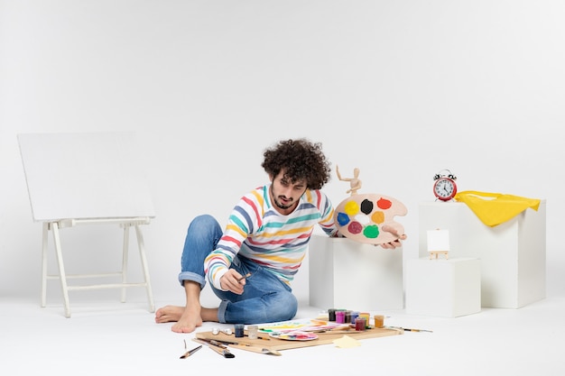 Vista frontal de las pinturas de dibujo de hombres jóvenes en la pared blanca